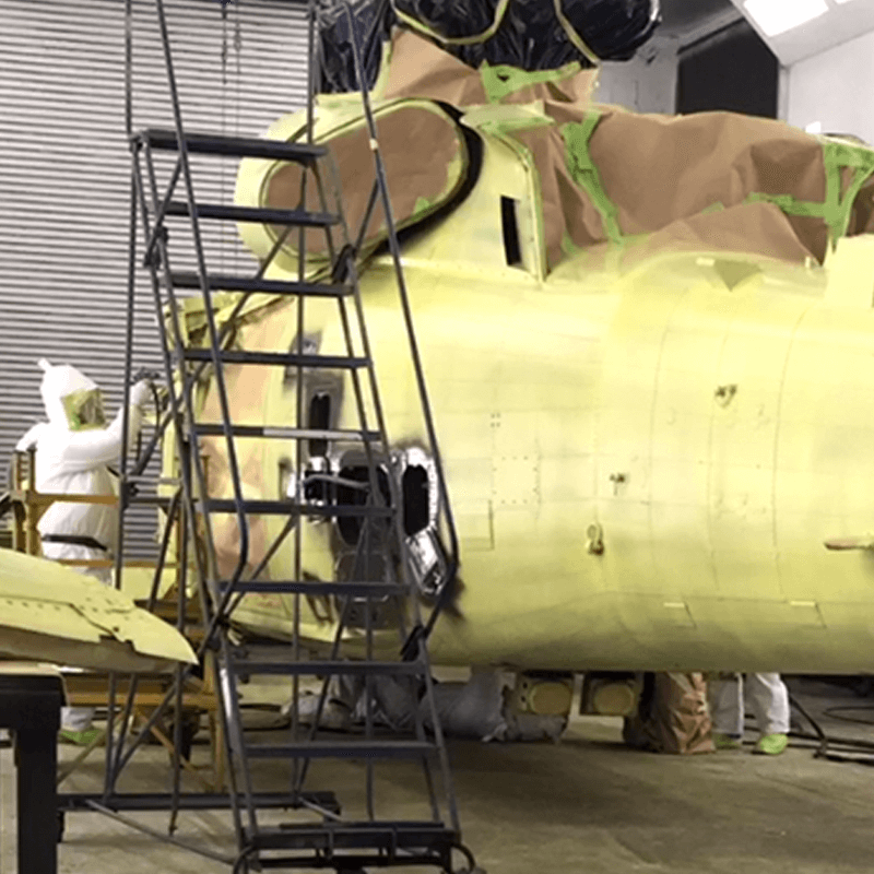 a military helicopter in a paint booth sits waiting to be repainted