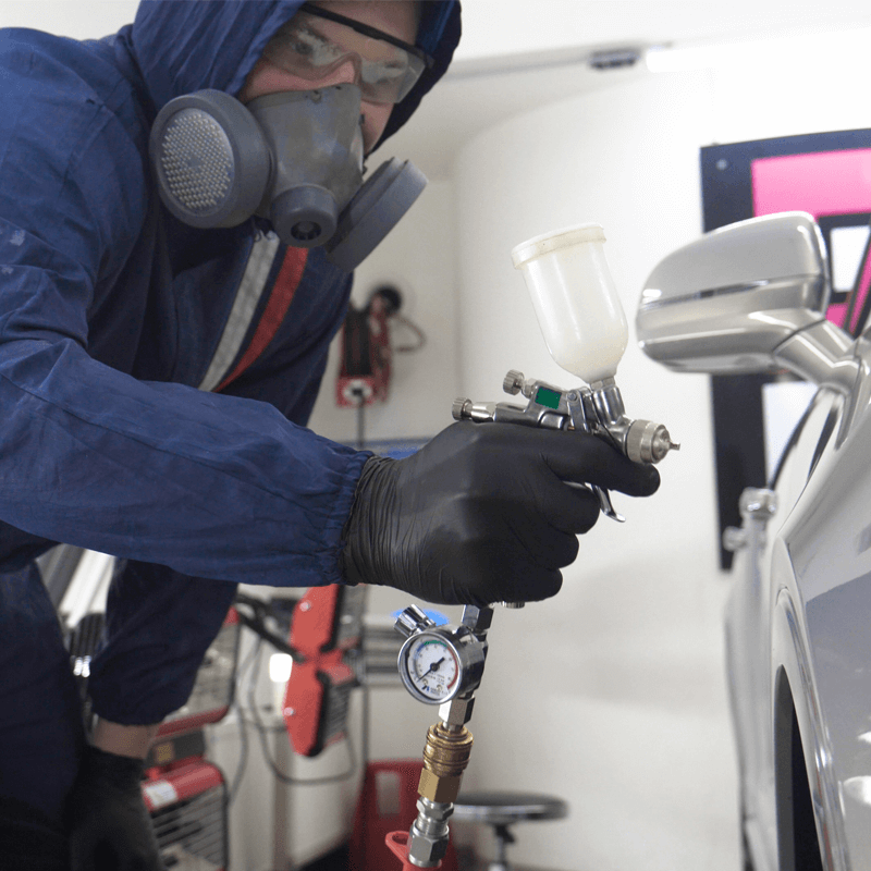 Spray booth painter wearing proper protection paints car