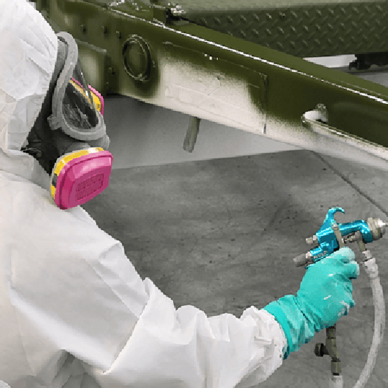 a painter trainee in proper safety gear practices spray application on a disassembled auto part