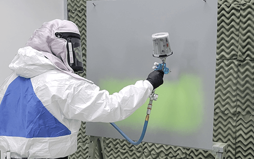 Painter trainee practices proper spray technique inside paint booth