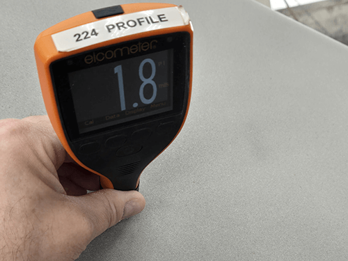 hand holding tool to measure thickness of blast paint on part