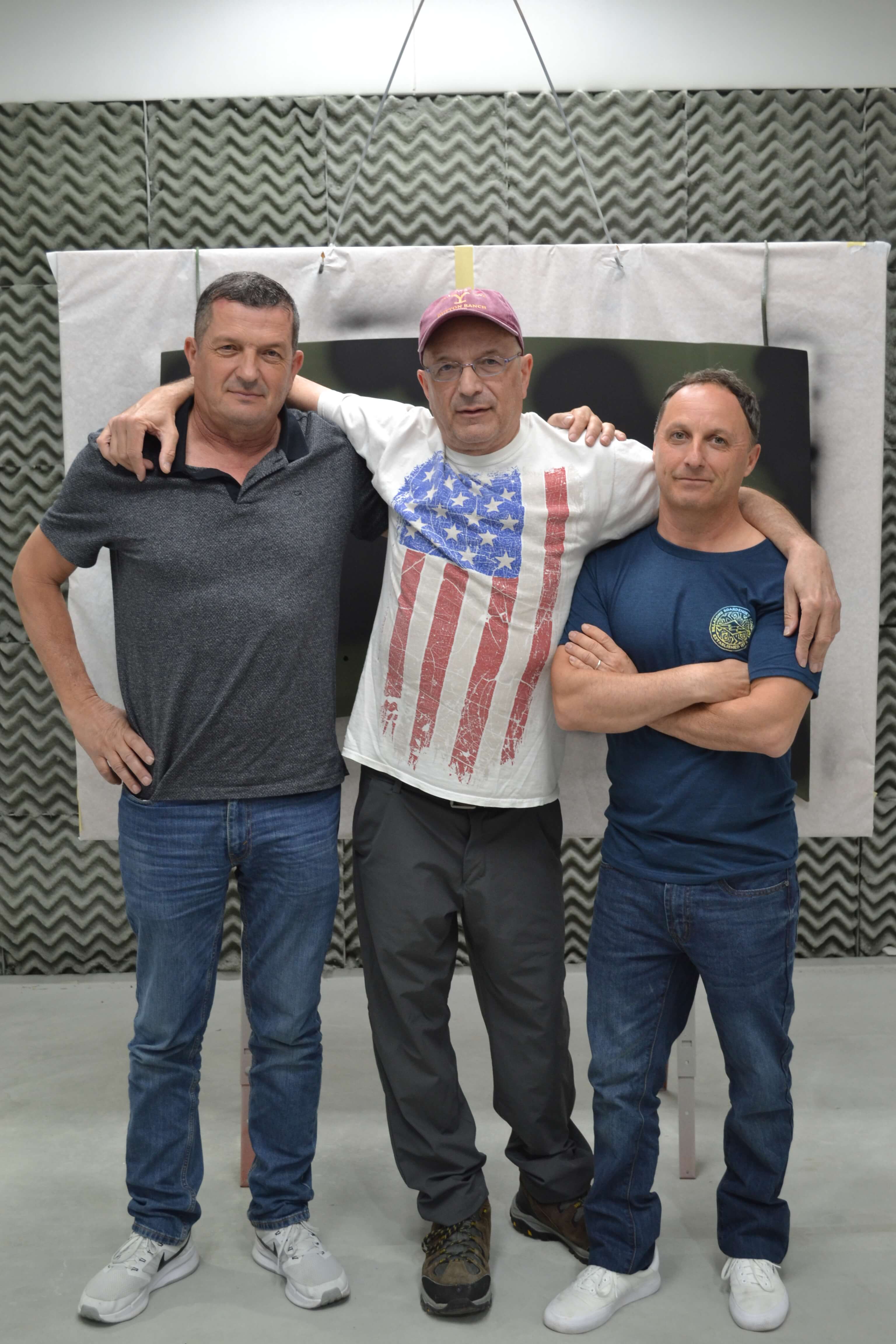 three men from Spain standing in paint booth in front of military asset