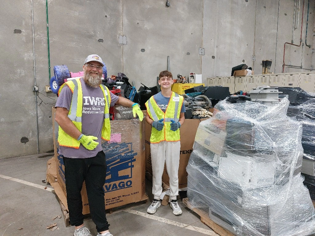 man and young boy with yellow safety vests standing in front of electronic waste items