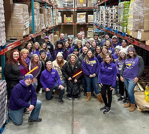 Large group all gathered in purple gear volunteering at the Northeast Iowa Food Bank