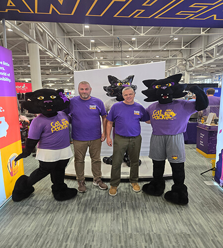 two purple and black panther mascots flanking two mean in khakis and purple t-shirts