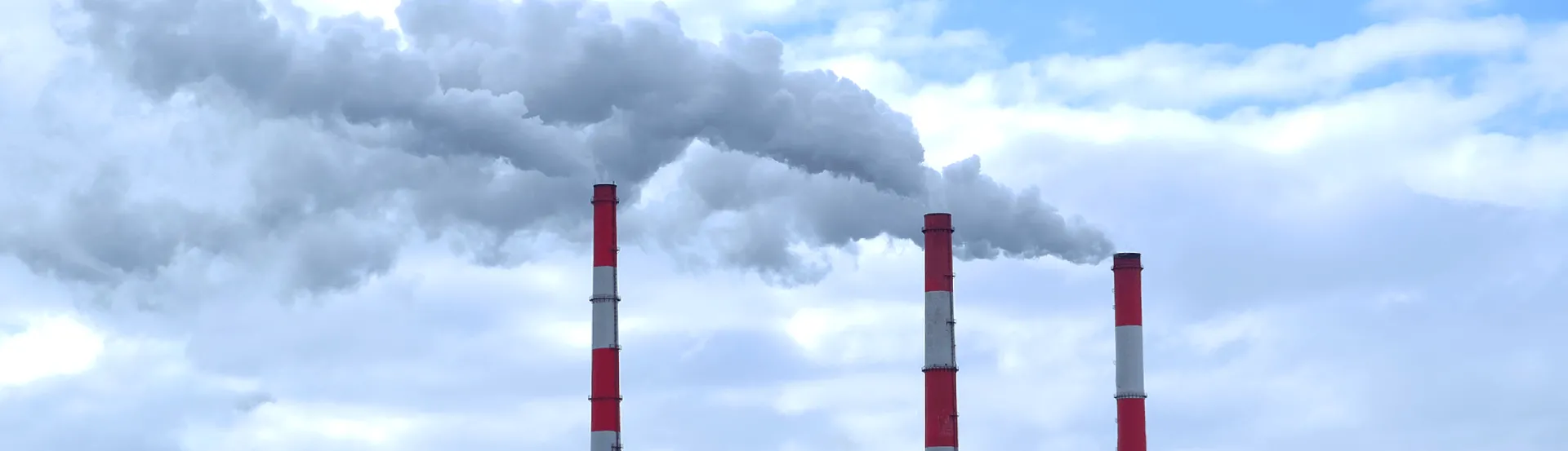 Three industrial smoke stacks expel smoke into atmosphere