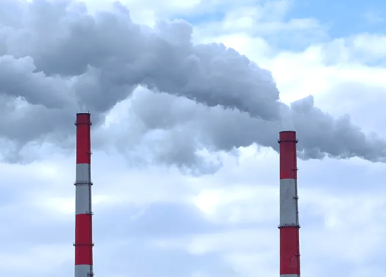 Three industrial smoke stacks expel smoke into atmosphere