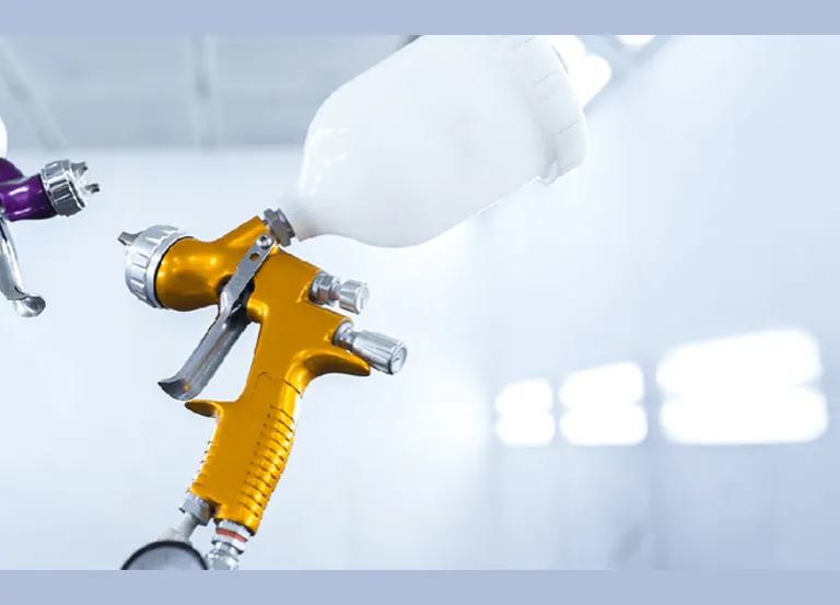 Two gravity feed paint guns used for painting vehicles shown inside spray booth