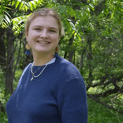 Environmental intern Makayla Gaspar stands before a green field of trees in springtime.