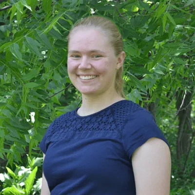 Student intern Eliana Hornbuckle stands before field of green trees and prairie grass.