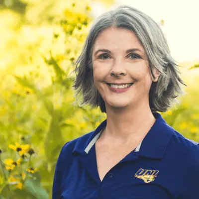 Link, Julie Reinitz standing before field of yellow flowers, profile page